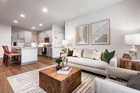 A modern living room with a white couch, a wooden coffee table, and a kitchen area in the background.