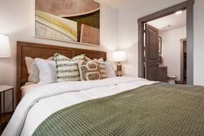 A bed with a green blanket and pillows in a room.