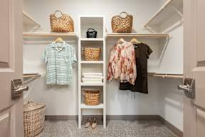 A white closet with clothes and baskets on shelves.