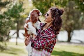 A woman in a plaid shirt is holding a dog in her arms.