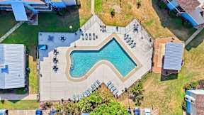 An aerial view of a swimming pool surrounded by a grassy area and a few buildings.