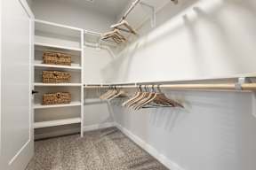 A white closet with clothes hanging and baskets on shelves.
