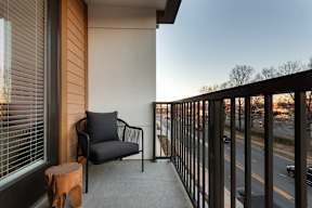 A chair and stool are on a balcony overlooking a street.