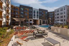 A sunny day at a modern apartment complex with a pool and outdoor furniture.