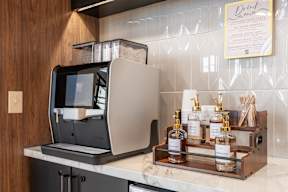 A coffee machine is on a counter with a tray of four bottles of syrup.