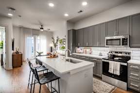 A modern kitchen with a white island and black chairs.