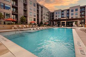 A swimming pool surrounded by sun loungers and apartment buildings.