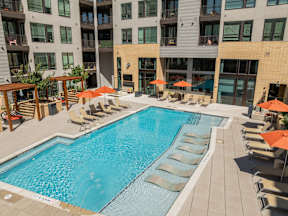 A large swimming pool surrounded by lounge chairs and umbrellas in front of a building.