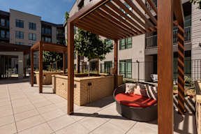 A wooden pergola provides shade over a seating area in a courtyard.