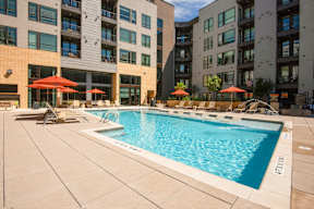 A swimming pool surrounded by buildings and umbrellas.