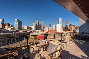 A rooftop patio with wooden furniture overlooking a city skyline.