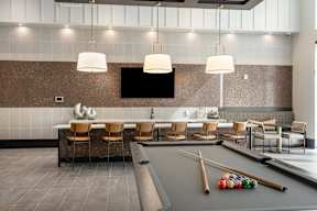 A billiard table with balls and cues is in the middle of a room with chairs and a television.