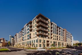 A large, modern building with many windows and balconies is situated on a street corner.