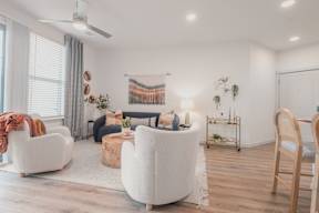 A living room with a white sofa, a white armchair, a white coffee table, a white rug, a white ceiling fan, a white wall, a white door, a white couch, a white chair, a white table