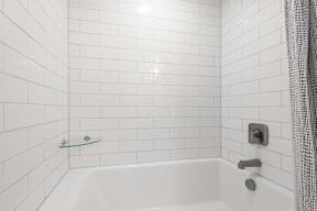 A white tiled bathroom with a white tub and a shower head.