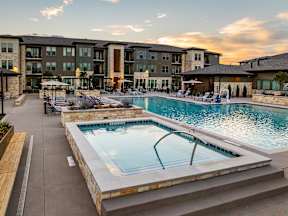A swimming pool surrounded by a stone wall and a patio area with chairs and umbrellas.