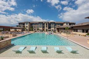 A large swimming pool with lounge chairs in front of a multi-story building.