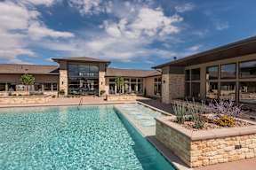 A swimming pool in front of a house with a stone wall.