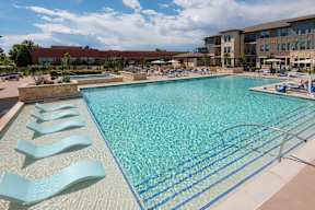A large swimming pool with lounge chairs and a building in the background.