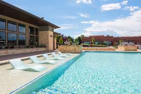 A pool with a blue tiled edge and white lounge chairs in front of a building.