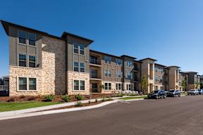 A row of modern apartment buildings with cars parked in front.