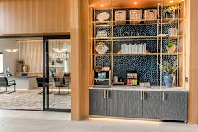 A modern interior with a glass door entrance, a grey cabinet, and a shelf with various decorative items.