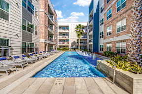 a swimming pool with chaise lounge chairs and palm trees in front of an apartment building at Republic at Alamo Heights, Texas
