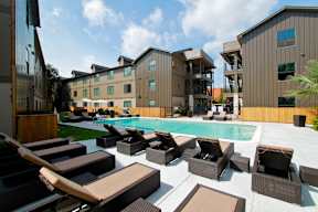 A pool area with lounge chairs and a building in the background.