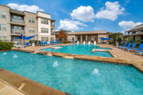 a swimming pool with blue lounge chairs and umbrellas in front of an apartment building