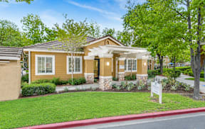 A house with a brown and beige exterior is surrounded by greenery and a red curb.