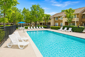 A swimming pool surrounded by white lounge chairs and trees.
