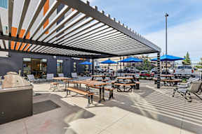 A sunny day at a covered outdoor seating area with tables and benches at The Orion Senior Apartments - Orange, CA Apartments, California