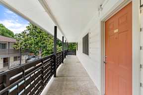 A long white covered walkway with a black railing and a red door at the end.