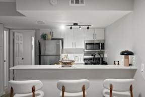 A modern kitchen with white chairs and appliances.