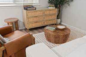 A living room with a white couch, a brown chair, a wooden cabinet, and a small tree.