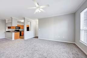 A spacious living room with a ceiling fan and a kitchen area in the background.
