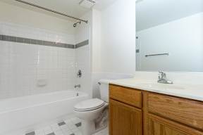 A white toilet sits in a bathroom with a white tub and a white sink.