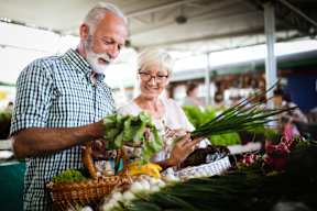 A man and a woman are shopping for vegetables at a market.