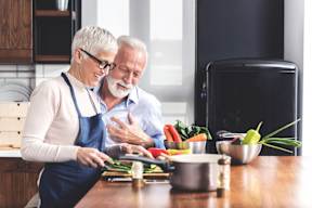 An older couple is preparing food together in a kitchen.