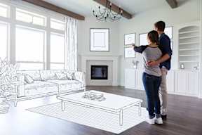 A couple is standing in a living room looking at a drawing on the wall.