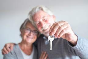 An elderly couple holding a key together.