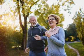 An older man and woman jogging in a park.