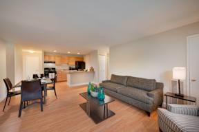 A living room with a grey couch and a dining table with chairs.