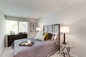 A bedroom with a bed, nightstand, and a window.