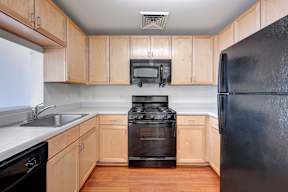 A black refrigerator sits in a kitchen with wooden cabinets.