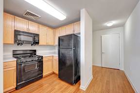 A black refrigerator sits in a kitchen with wooden cabinets and a black stove.