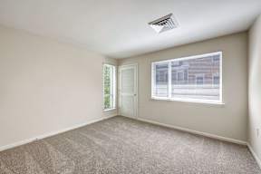 A room with a carpeted floor, a window with blinds, and a door leading to another room.