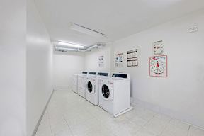 A laundry room with three washing machines and a white wall.
