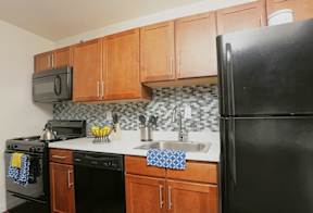 A black refrigerator stands in a kitchen with wooden cabinets and a black microwave. at Dominion Towers Apartments, Arlington, VA, 22204