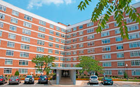 A large red brick building with a parking lot in front at Dominion Towers Apartments, Arlington, VA